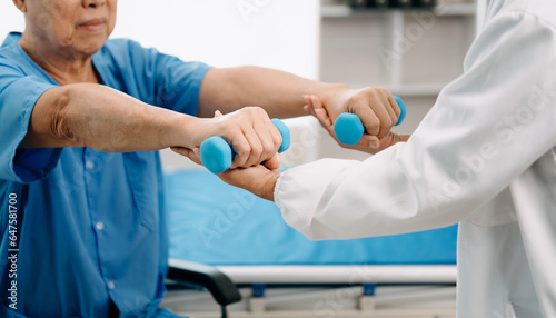 Asian physiotherapist helping elderly man patient stretching arm during exercise correct with dumbbell in hand during training hand in bed in clinic © Nuttapong punna