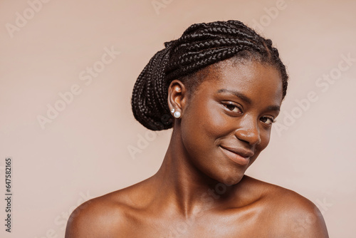 Beauty portrait of african girl with clean healthy skin over beige background. Smiling female with black braided hair, top knot hairstyle.