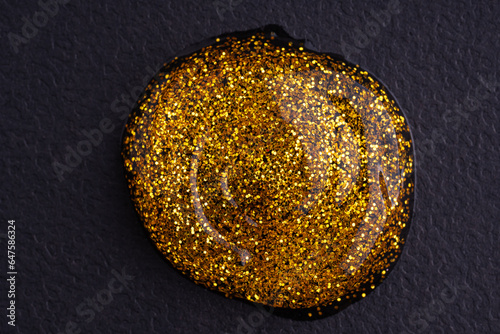 Round swatches of golden glitter paint on black paper background.