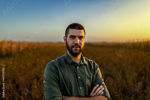 Portrait of young farmer standing in a soy field at sunset looking at camera.