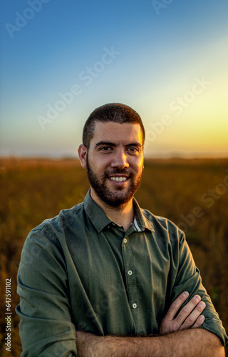 Portrait of young farmer standing in a soy field at sunset looking at camera.
