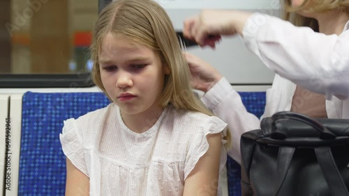 Mom combs her daughter in the subway. 