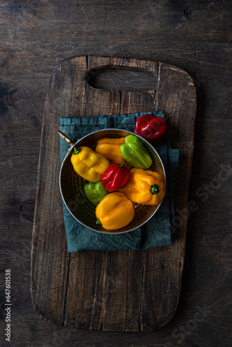 Overhead view of a bowl of red, yellow and green Scotch bonnet peppers on a chopping board photo