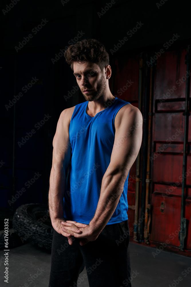 confident man in sportswear looking at camera and stretching arms on city street at night confident man in sportswear looking at camera and stretching arms on city street at night