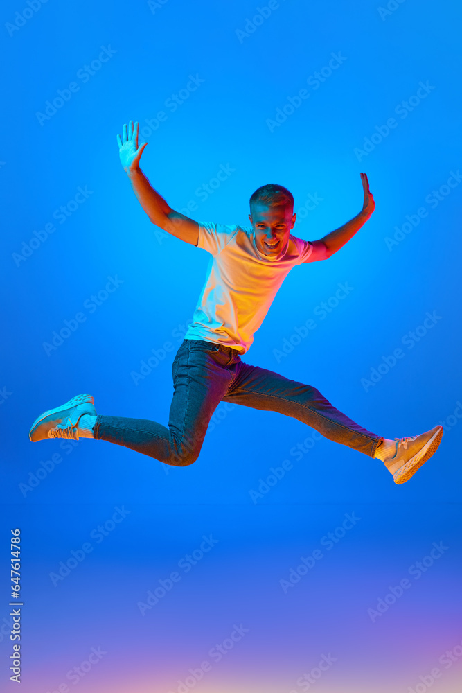 Obraz premium Neon light portrait of victorious delighted jumping man raising hands in star shape, shouting for joy, celebrating win success, thrilled emotions.