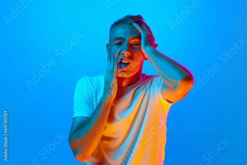 Φωτογραφία Portrait of young man, student on blue studio background in neon light, tired co
