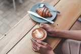 Close up of a hand holding a cup of coffee latte on a wooden table
