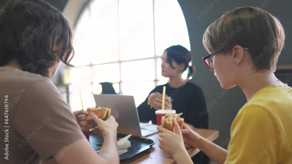 group of students sit in a cafe and do a project on lifestyle a laptop together. business concept of modern training and development. students discuss their homework and eat fast food burgers