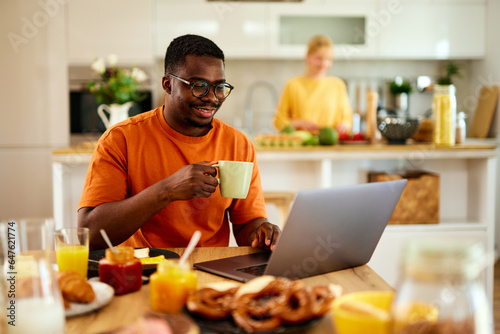 African American man using laptop while enjoying breakfast at home