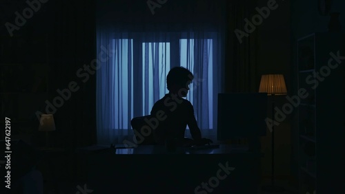 Everyday life creative concept. Man sitting at the desk in the dark room and working on pc.