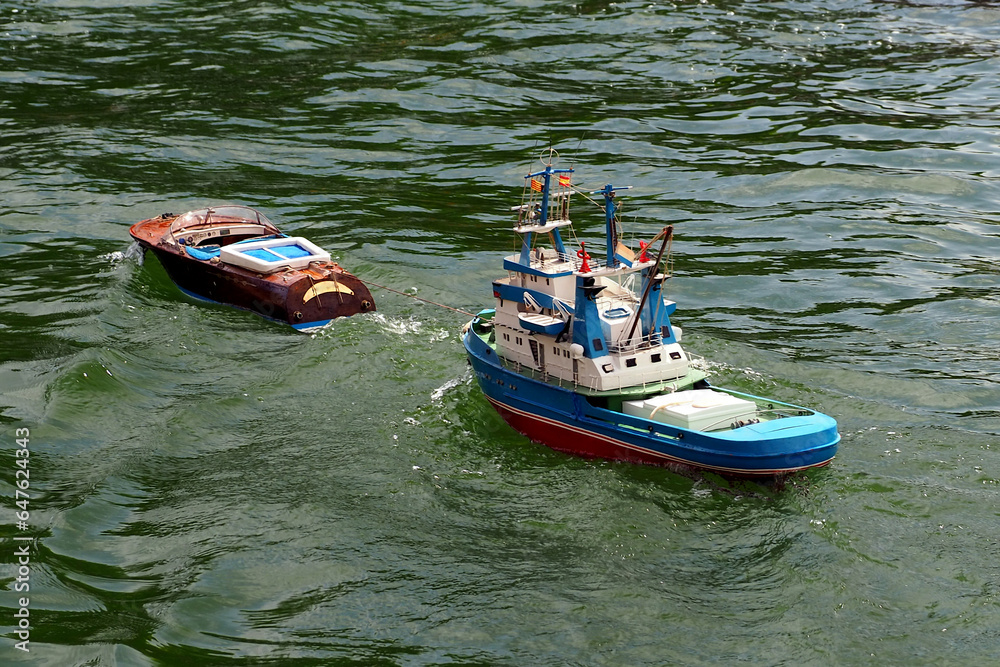 A small radio-controlled fishing boat is towed by a RC patrol ship A small radio-controlled fishing boat is towed by a RC patrol ship