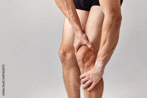 Knee pains. Cropped image of muscular, relief male legs against grey studio background. Model in underwear. Medical treatment. Concept of men's health and beauty, body care, fitness, wellness, ad