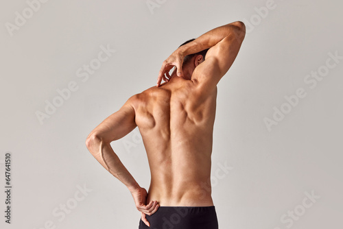 Back massage. Muscular, relief, strong male back against grey studio background. Model posing in underwear. Concept of men's health and beauty, body care, fitness, wellness, ad