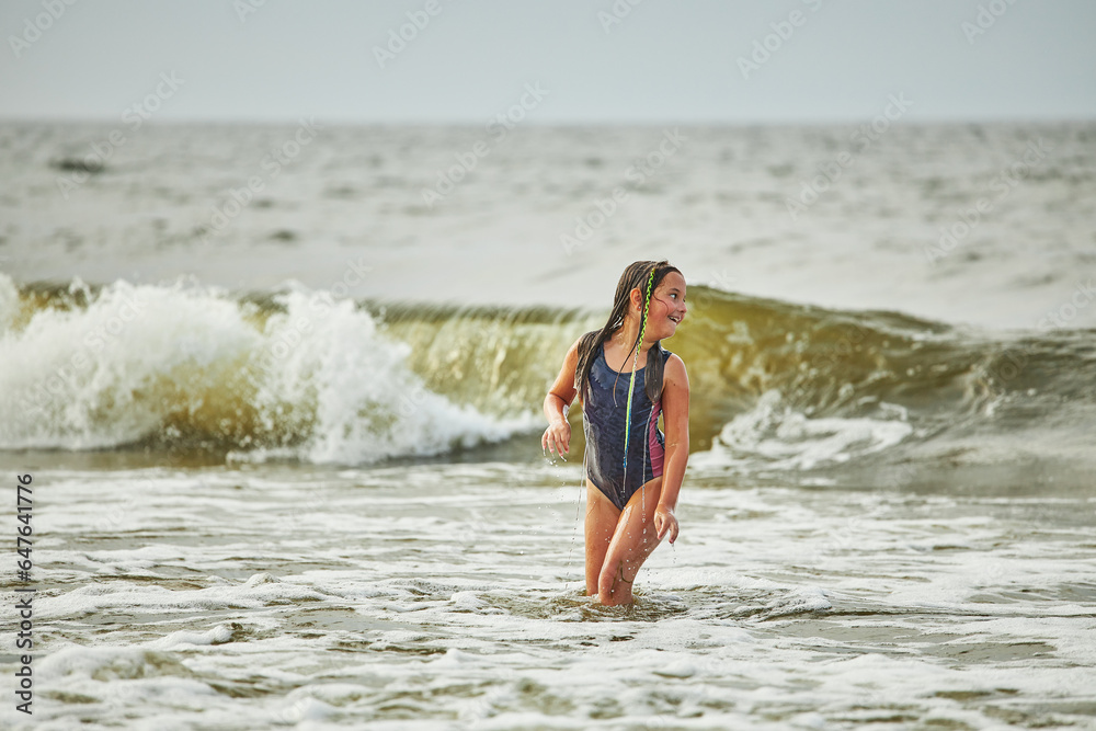 Little girl playing with waves in the sea. Kid playfully splashing in waves. Child jumping in sea. Vacations on the beach. Water splashes Little girl playing with waves in the sea. Kid playfully splashing in waves. Child jumping in sea. Vacations on the beach. Water splashes