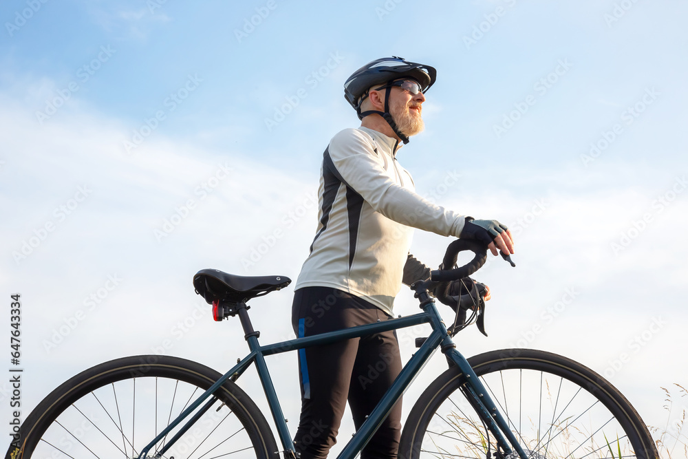 Naklejka premium Bearded man cyclist stands with a bike against the blue sky. cycling and health hobbies