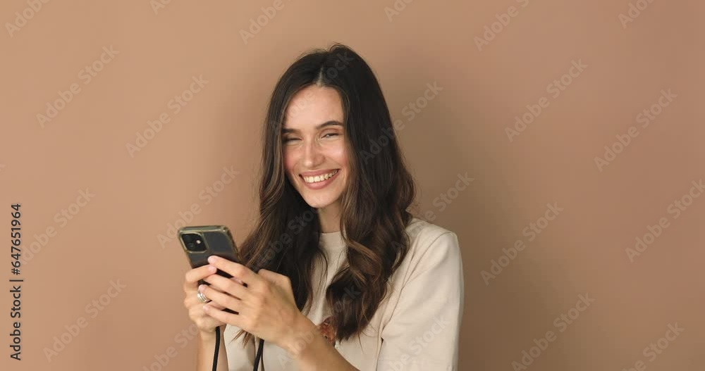 Great application or website. Excited woman using her mobile phone, isolated on beige studio background. Positive lady holding gadget, looking at camera, texting, messaging. Great application or website. Excited woman using her mobile phone, isolated on beige studio background. Positive lady holding gadget, looking at camera, texting, messaging.