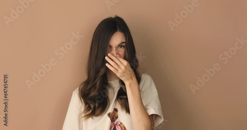 Disgusting odor. Discontent brunette curly woman frowning face, smells something awful, feeling aversion, beige studio background. Girl face with aversion dislikes something unpleasant show thumb down photo