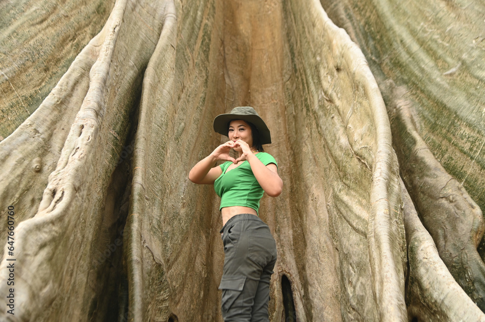 Fototapeta premium Pretty Asian woman Cheerful and happily at the base of a big tree. And this tree is very large and is a popular attraction for Thai tourists. Located at Uthai Thani Province in Thailand.