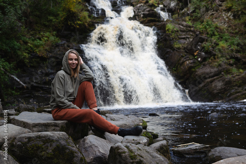 a young beautiful woman tourist sitting against the backdrop of a waterfall surrounded by forest