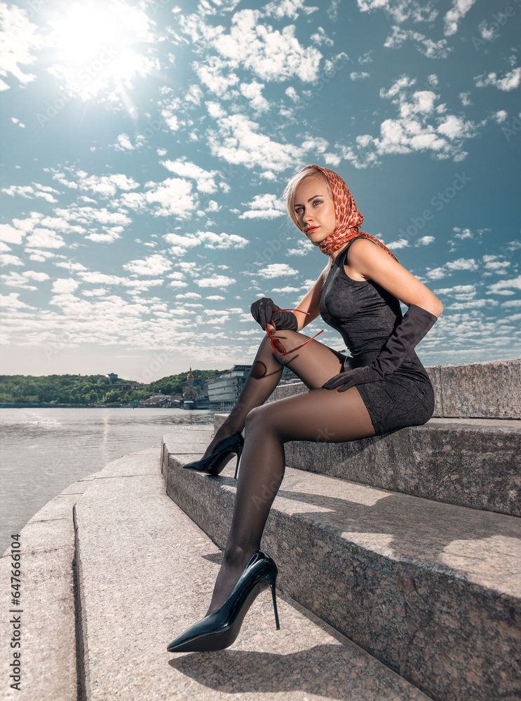 Beautiful blonde girl in black dress with perfect legs in pantyhose and