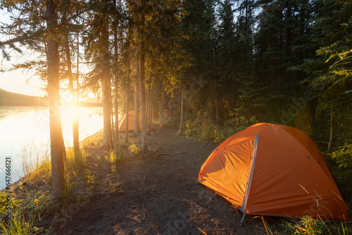 orange tent in a forest at the Yukon River in Canada during epic sunset