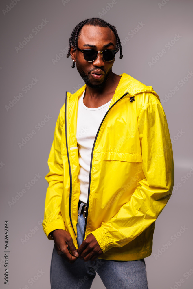 Charismatic african american man in sunglasses wearing bright yellow windbreaker jacket isolated on grey Charismatic african american man in sunglasses wearing bright yellow windbreaker jacket isolated on grey