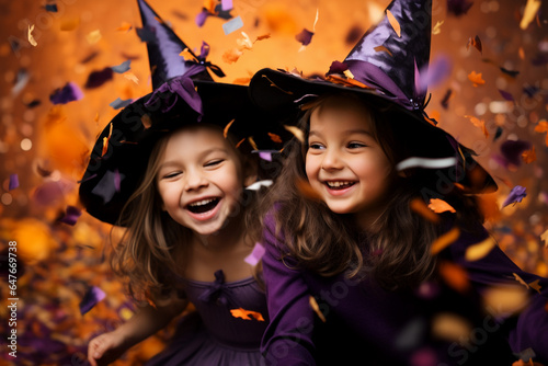  little girls in Halloween witch costume on orange background with flying confetti, candid