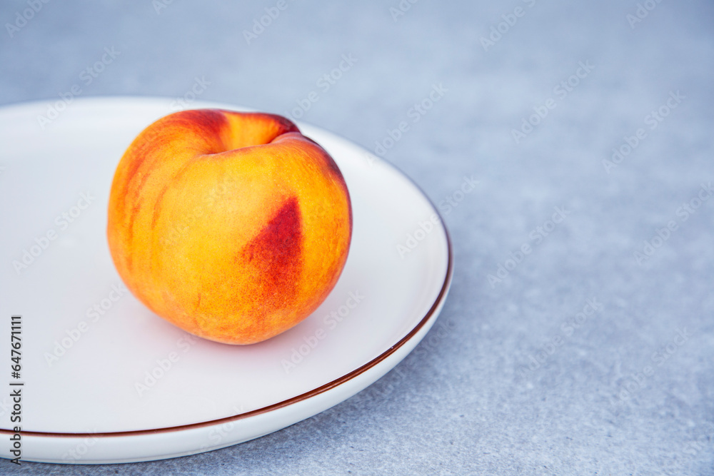 Ripe peach on a white plate on a gray background, close up Ripe peach on a white plate on a gray background, close up