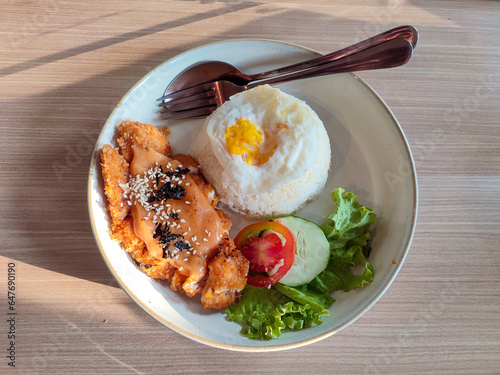 Breakfast menu with side dishes of mentai chicken, fresh vegetables and fried eggs on a table exposed to sunlight coming through the window. Negative space