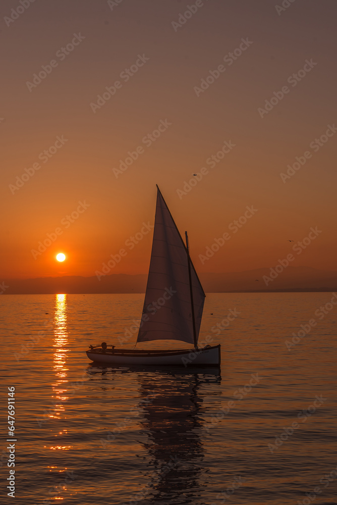 View of a sailboat sailing on the lake at sunset.