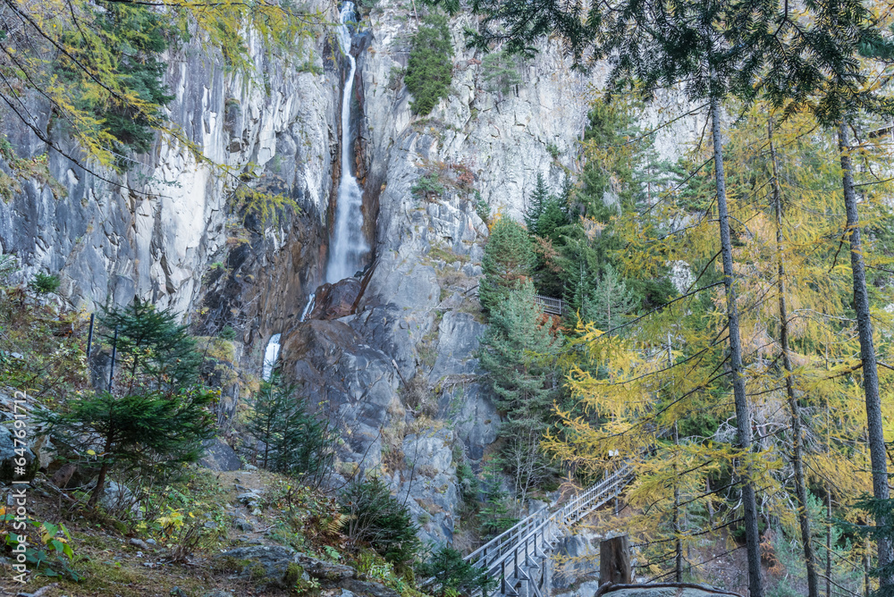 Obraz premium Wooden footpath and waterfall on a rocky mountain in a forest on an autumn day.