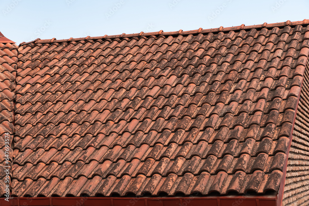 Red terracotta ceramic tiles on the roof over the brick wall of a residential building. Diagonal pattern, wavy shape. Traces of dampness and black mold Red terracotta ceramic tiles on the roof over the brick wall of a residential building. Diagonal pattern, wavy shape. Traces of dampness and black mold