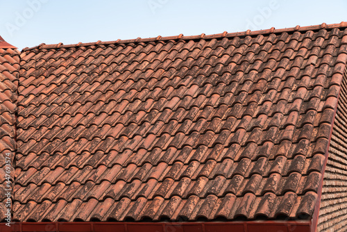Red terracotta ceramic tiles on the roof over the brick wall of a residential building. Diagonal pattern, wavy shape. Traces of dampness and black mold