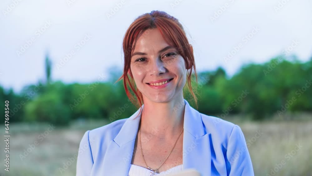 portrait of a young woman working remotely sitting on lawn in park among trees, smiling and looking at camera portrait of a young woman working remotely sitting on lawn in park among trees, smiling and looking at camera