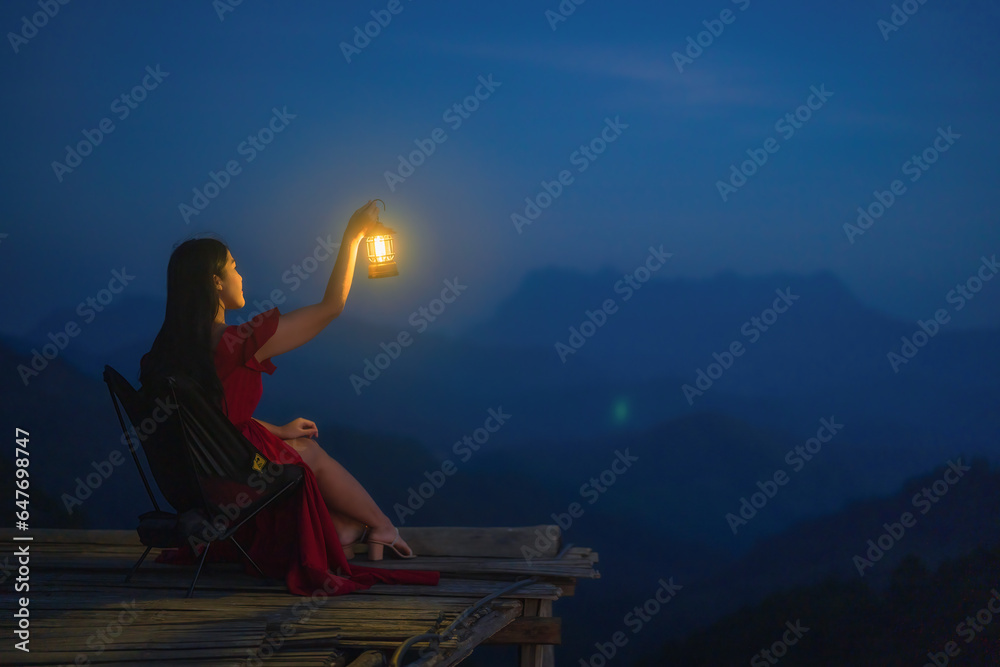 A woman sitting with a lantern in the night on the mountain.