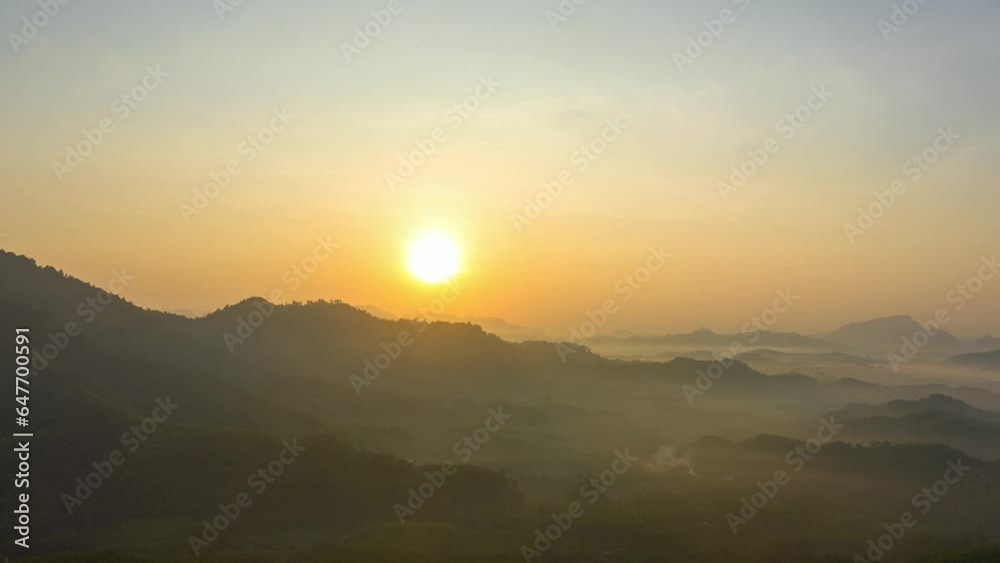 Aerial hyperlapse The sun gradually sets over the mountain..The sky is painted with streaks of yellow and orange..The fading light casts a gentle glow on the fog.