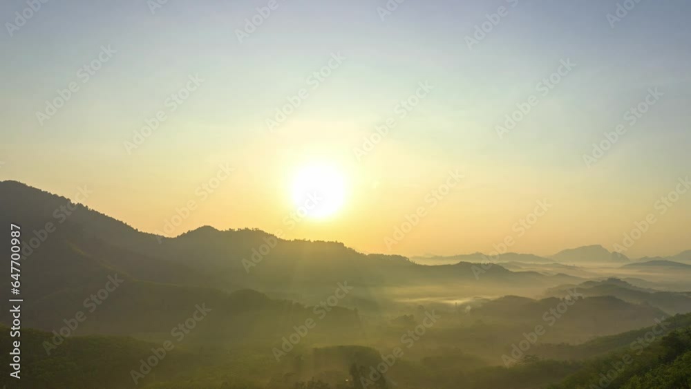 Aerial hyperlapse The sun gradually sets over the mountain..The sky is painted with streaks of yellow and orange..The fading light casts a gentle glow on the fog.