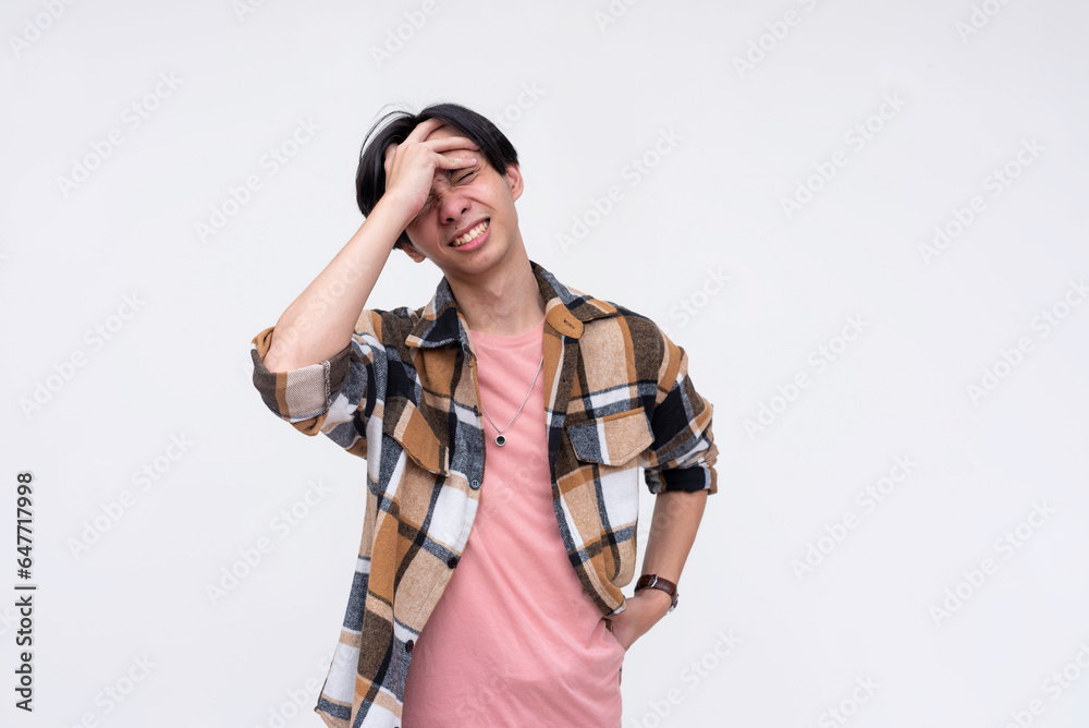 A young frustrated asian man face palms from stress. Screwing up and realizing his blunders. Annoyed by incompetent employees. Mental health concept. Isolated on a white background. A young frustrated asian man face palms from stress. Screwing up and realizing his blunders. Annoyed by incompetent employees. Mental health concept. Isolated on a white background.