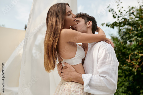 Fotografija passionate couple, man seducing sexy woman while standing near white tulle of pa