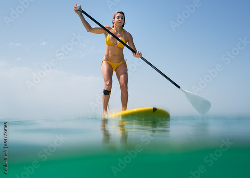 A woman in a yellow bikini paddles on a yellow board; Tarifa cadiz andalusia spain photo