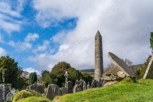 Medieval ruined graveyard with round tower in sunshine at churchyard in Glendalough's monastic town. Early medieval monastic settlement founded by St Kevin in the 6th century