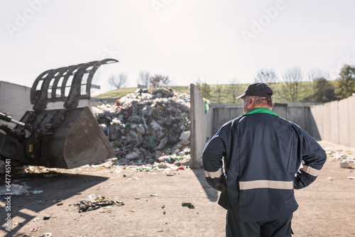 Recycling center worker, in dark blue work clothes, looking at an unsorted garbage heap just arrived in the materials recovery facility
