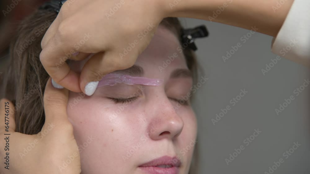 Correction of eyebrow shape with hot wax close-up. An eyebrow artist applies wax to the eyebrow of a woman's face and removes the hardened pink wax. Wax correction of eyebrow shape Correction of eyebrow shape with hot wax close-up. An eyebrow artist applies wax to the eyebrow of a woman's face and removes the hardened pink wax. Wax correction of eyebrow shape