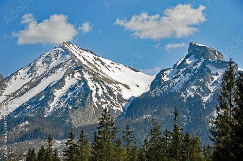 Dwa ośnieżone szczyty górskie: Mały Wierch i Hawrań w Tatrach Bielskich, na tle niebieskiego nieba z kilkoma obłokami.