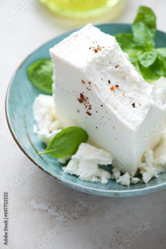 Turquoise bowl with a block of feta cheese and green basil, vertical shot, close-up, selective focus