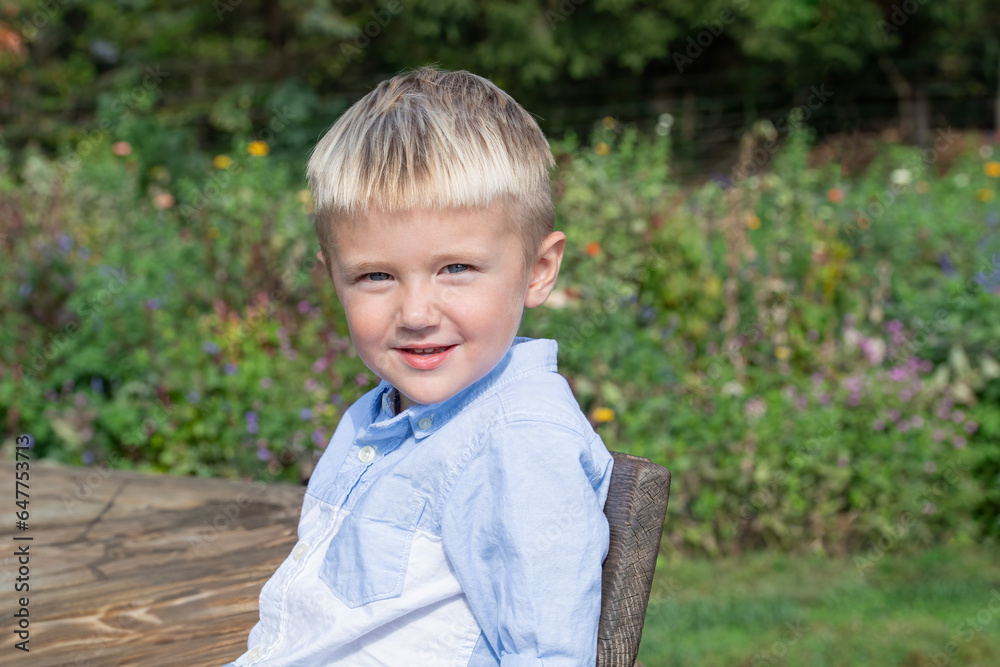 Blonde haired blue eyed boy sits on a bench outside in a garden Blonde haired blue eyed boy sits on a bench outside in a garden