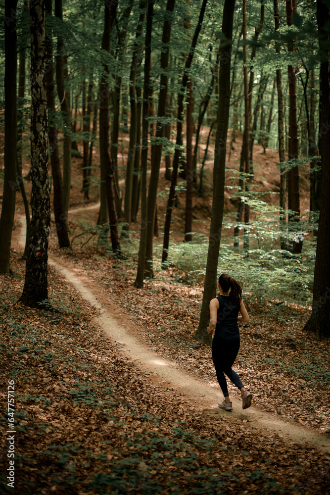 Rare view of young woman running on narrow forest path against tall trees landscape Rare view of young woman running on narrow forest path against tall trees landscape