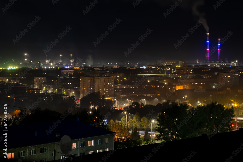 The night landscape of the city. Beautiful urban area with houses and boiler room at night. View of the big city from above. Smoking chimneys of boiler rooms on the background of the cityscape.