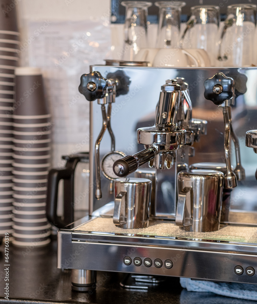 The barista prepares fresh coffee in the coffee machine in the morning in the cafe. There are coffee cups on the table for customers. Coffee machine close-up
