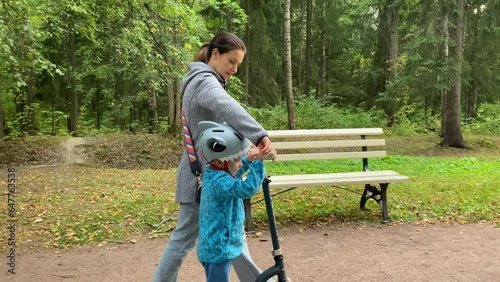 mother and toddler child little boy ride a scooter in the park. Aleksandrovsky Park, Pushkin, St. Petersburg, Russia. photo